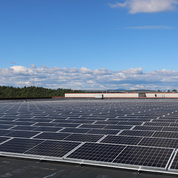 Far view of a field of solar panels with a blue sky and clouds in the background.